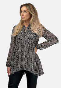 Czarna i biała kwiatowa bluzka z długimi rękawami, dekoltem w kształcie łezki i luźną, zwiewną sylwetką, zestawiona z dopasowanymi czarnymi spodniami.