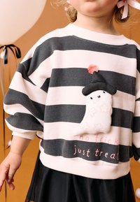 Felpa a righe in morbido cotone, con un fantasma bianco che indossa un cappello nero e un pompon rosa, testo ricamato "niente trucchi, solo dolcetti."