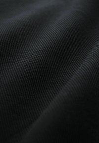 Tissu noir avec une fine texture côtelée verticale et des plis doux créant des ondes légères à travers la surface.