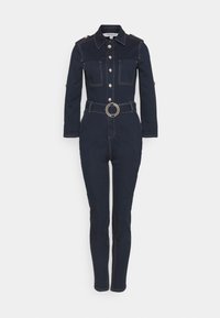 Combinaison en denim foncé à manches longues avec fermeture à boutons sur le devant, poches poitrine, taille ceinturée avec boucle circulaire, et jambes étroites et fuselées.