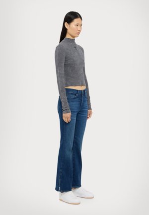 Grå långärmad croppad t-shirt med en subtil textur, tillsammans med blå flare jeans med lätt slitage och vita sneakers.