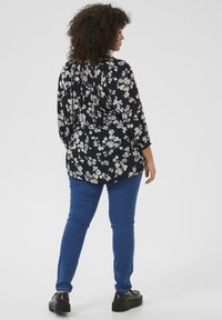 Blouse à imprimé floral avec encolure froncée, manches longues et coupe fluide, associée à un jean slim bleu et à des chaussures à plateforme noires.