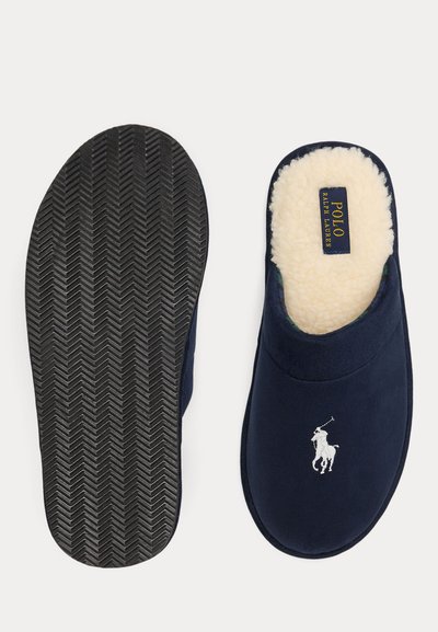 Zapatilla azul marino con logo bordado en blanco, forro de forro polar y suela de goma negra texturizada, mostrada desde vistas superior e inferior.