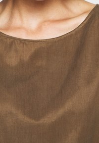 Detailní záběr na krk a oblast klíční kosti osoby, která má na sobě hnědý, kulatý výstřih z látky.