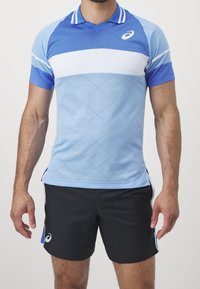 Niebieska koszulka sportowa z krótkim rękawem, w rombowy wzór i białą poziomą paskiem. Połączona z czarnymi szortami z bocznymi akcentami.
