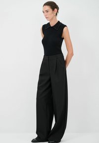 Svart ribbad ärmlös topp med krage prydd med nitar, i kombination med högmidjade, vida svarta byxor. Slät tygkvalitet, minimalistisk design.