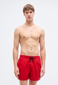Κόκκινα μαγιό βερμούδα με ελαστική μέση και μαύρο κορδόνι, με ομαλή υφή και σχεδιασμό μήκους ως το μέσο του μηρού.