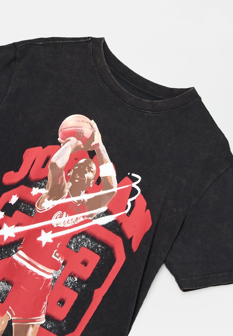 T-shirt in cotone nero con un'immagine di un giocatore di basket, che indossa una maglia rossa con accenti bianchi, e testo in rosso e bianco in grassetto.