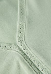 Tessuto verde chiaro con una texture liscia, caratterizzato da una rifinitura ondulata dettagliata e piccoli fori lungo la cucitura per un design aggiuntivo.