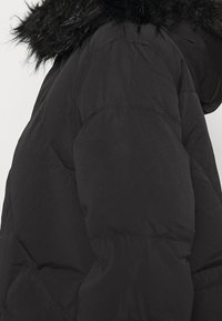 Černá péřová bunda s umělým kožíškem na kapuci, s prošívaným designem a texturovanou tkaninou. Rukávy jsou mírně naškrobené na manžetách.
