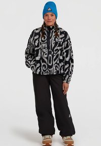 Mustriline mustvalge fliisjakk lukuga, millel on sinine müts ja mustad püksid. Näha on tekstuuriga kangas ja kolmnurkse logoga detail.