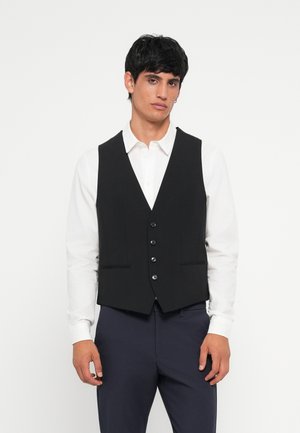 Schwarze Weste mit taillierter Passform, mit V-Ausschnitt, fünf Knöpfen und zwei vorderen Taschen, getragen über einem weißen Hemd und blauen Hosen.