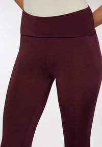 Leggings bordeaux con una cintura ampia e elastica. Realizzati in materiale liscio e leggero, con una forma aderente e senza motivi visibili.