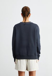 Mörkblå sweatshirt med avslappnad passform, rund halsringning med vit kant och ribbade ärmslut. Matchas med ljusfärgade, texturerade shorts.