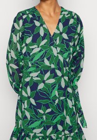 Sukienka w stylu wrap w granatowym kolorze z zielono-białym kwiatowym wzorem. Długie rękawy, dekolt w kształcie litery V oraz regulowane troczki w talii. Lekki materiał.