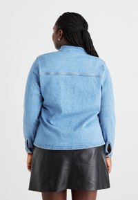 Gai zila džinsa jaka ar klasisku apkakli, garām piedurknēm un aproces atverēm, apvienota ar melnu ādas svārku. Vienkārša dizaina detaļas.