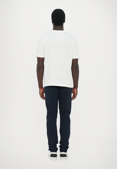 T-shirt en coton blanc à manches courtes, associé à un pantalon slim-fit bleu marine. Les chaussures présentent une base blanche et un accent noir au niveau du talon.
