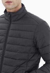 Giacca nera imbottita con colletto alto, design trapuntato, logo discreto e chiusura lampo, realizzata in materiale liscio e leggero.