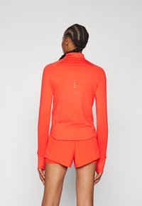 Rode sportieve lange mouwen top met een hoge kraag en duimgaten, gecombineerd met bijpassende shorts. Bevat reflecterende accenten op de achterkant.