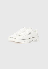 Sneaker bianco con tomaia in pelle liscia, dettagli forati, design con lacci e suola spessa e texture caratterizzata da motivi ritagliati.