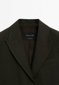 Col du veston de costume brun foncé avec revers et poche poitrine, montrant l'étiquette Massimo Dutti à l'intérieur du col.