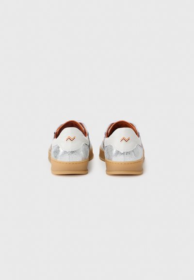 Sneakers with a silver metallic finish on the heel, white upper, and brown soles. Features a zigzag accent in orange stitching.