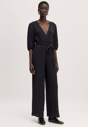 Combinaison noire avec un décolleté plongeant, tissu texturé, design à jambes larges et taille nouée. Comprend des manches bouffantes à longueur de coude et une couleur unie.