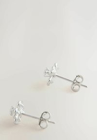 Cercei tip stud în formă de floare argintie, cu accente de cristale clare, având un finisaj metalic neted și un design tradicional cu închidere tip post.