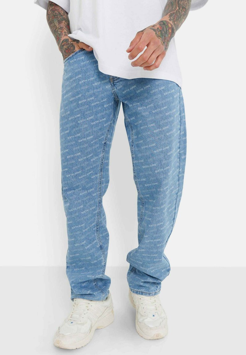 Jeans de denim de color azul claro con un patrón repetido de texto "SIXTH JUNE", corte relajado, acabado ligeramente desteñido, combinados con zapatillas blancas.