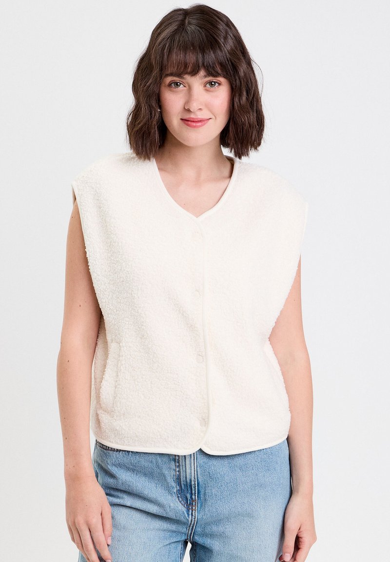 Gilet sans manches en polaire blanche avec un col en V, une fermeture à boutons à l'avant et des poches latérales. Texture douce et finition arrondie en bas.
