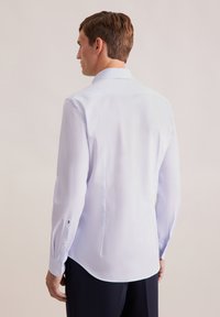 Camicia a maniche lunghe azzurra chiara con un motivo sottile, vestibilità su misura e polsini abbottonati. Presenta un colletto classico e un orlo curvo.