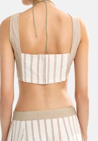 Lnianowy crop top z kwadratowym tyłem, z pionowymi czerwonymi i niebieskimi paskami na beżowym tle. Zawiązywany na szyi kolorowym plecionym sznurkiem.