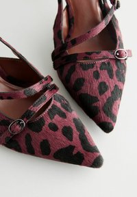 Leopard print heels with a pointed toe, featuring purple and black fur-like texture, crisscross straps, and a silver-tone accent buckle.
