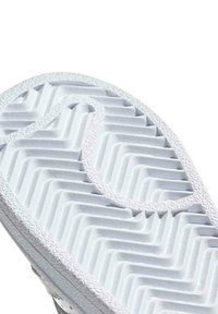 Semelle de sneaker blanche avec un motif en chevrons, surface texturée et bords lisses. Présente un design distinct en forme de boucle au centre.