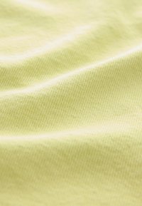 Tejido amarillo claro con una textura suave, que presenta un sutil patrón tejido y suaves ondas, indicando elasticidad y comodidad.