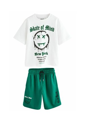 Witte katoenen t-shirt met groene grafische print met een glimlachend gezicht en tekst. Groene shorts met trekkoord, zijzakken en logo.