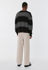 Crna i siva prugasta pulover s opuštenim krojem, rebrastom teksturom, spuštenim ramenima, nosi se s bež širokim hlačama i crnim cipelama.