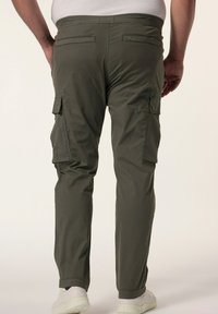 Vihreät cargo-housut, joissa on kapea istuvuus, useita sivutaskuja ja sileä pinta, yhdistetty valkoisiin kenkiin.