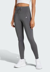 Gray high-waisted leggings made of stretchy fabric with a smooth texture, featuring a drawstring waist and reflective logo detail.