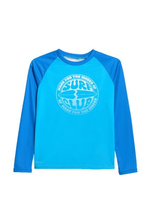 Długi niebieski rash guard z ciemniejszymi niebieskimi rękawami i białym, okrągłym logo klubu surfingowego na środku z przodu.