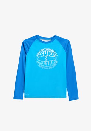 Długi niebieski rash guard z ciemniejszymi niebieskimi rękawami i białym, okrągłym logo klubu surfingowego na środku z przodu.