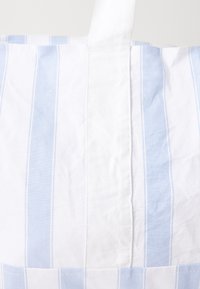 Sacola de tecido riscada com listras verticais brancas e azuis claras alternadas, com uma alça superior branca e uma superfície ligeiramente texturizada.
