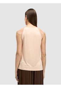 Vaaleanpunainen hihaton toppi, jossa on pitsikoristeet hartioilla, sileä kangas ja hieman pyöreä pääntie.