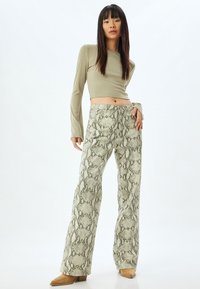 Pantalons à jambe large en imprimé serpent texturé, avec des verts et des bruns atténués, associés à un haut ajusté à manches longues en beige clair.