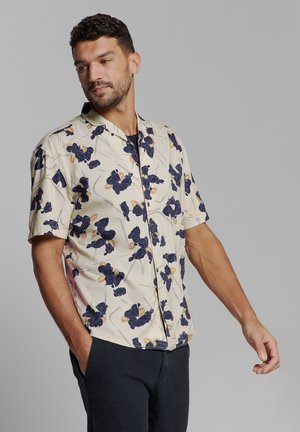 Korte mouwen knoopsluiting shirt in crème met blauw bloemenpatroon. Gemaakt van lichte stof, heeft een relaxed fit en een borstzak.