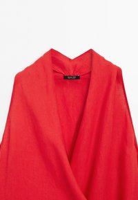 Czerwona lniana odzież bez rękawów z głębokim dekoltem w kształcie litery V i czarną metką z napisem Massimo Dutti wewnątrz kołnierza.