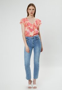 Bloemengepatroneerde top met gerimpelde mouwen in roze en oranje, gecombineerd met high-waisted lichtblauwe jeans en witte open teengympen.
