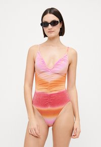 Maillot de bain une pièce dégradé de rose, orange et rouge avec des détails froncés et des bretelles fines ajustables, complété par une texture scintillante.
