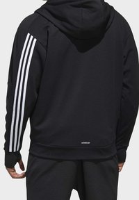 Svart huvtröja i texturerat tyg, med tre vita ränder på vänstra ärmen och "AEROREADY"-etikett vid fållen.