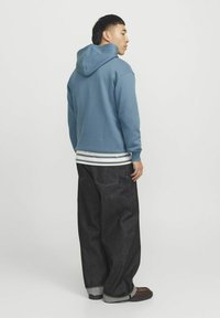 Blå bomulds hættejakke med en frontlomme, lagt over en hvid og grå stribet skjorte, parret med mørke denim brede bukser.
